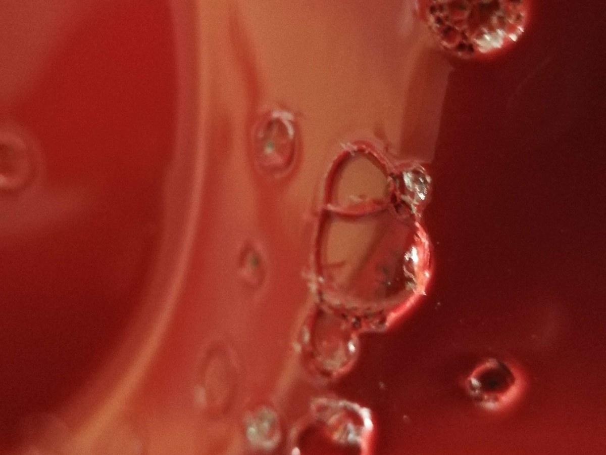 Close-up of bubbles and adhesion defects on a painted red composite surface.